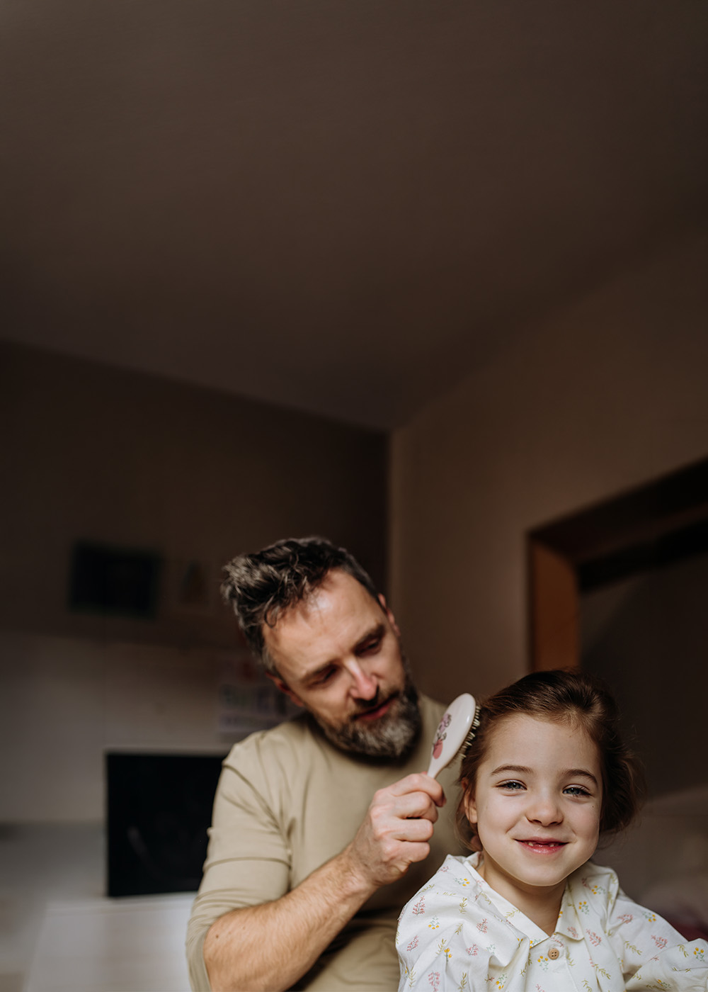 Kampania wizerunkowa w M1 Poznań - Bliżej niż myślisz - Tu poznali się moi rodzice. Obraz przedstawiający uśmiechniętego ojca robiącego fryzurę swojemu dziecku