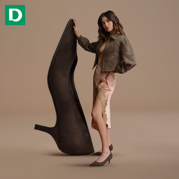 Grafika promocyjna DEICHMANN CHOCOLATE BROWN. Brunetka stojąca na beżowym tle i ogromny but na obcasie.