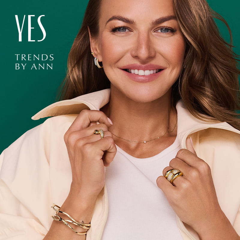 Grafika promocyjna marki biżuterii YES. Anna Lewandowska na zielonym tle reklamująca akcję Trends by Ann, nosząca złotą biżuterię; pierścionki, bransoletkę i kolczyki od Yes.